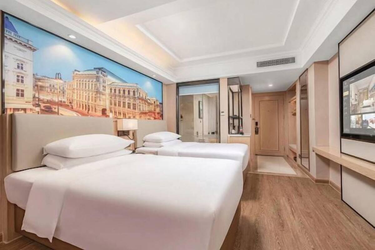 A hotel room with a large bed, a TV, a painting of a cityscape, and a wooden floor.