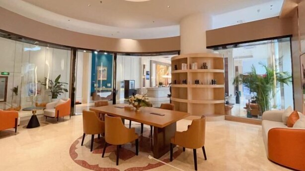A modern hotel lobby with a round table, orange chairs, a central bookshelf, and a glass wall offering a view of the interior. - Vienna International Hotel Foshan Qiandenghu Guicheng Subway Station Branch (Foshan)
