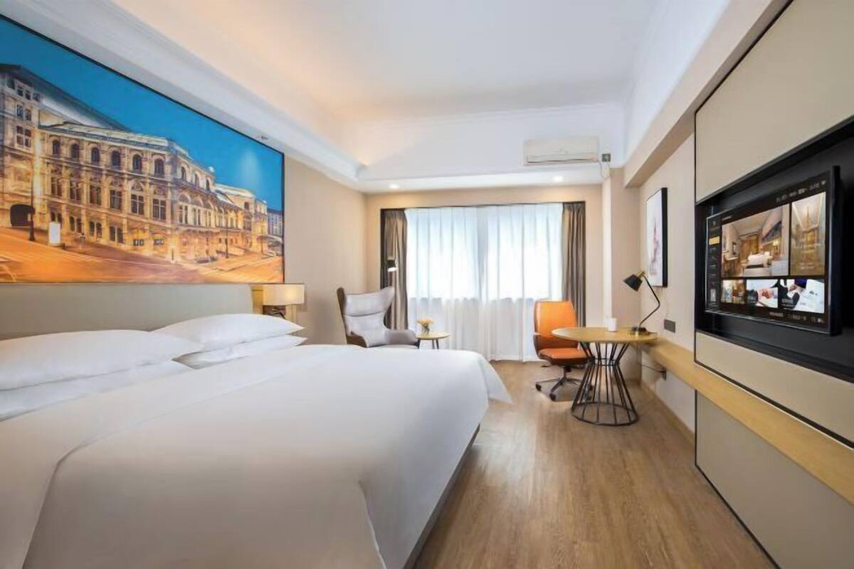 A hotel room with a large bed, a desk with a chair, a television, and a painting on the wall.
