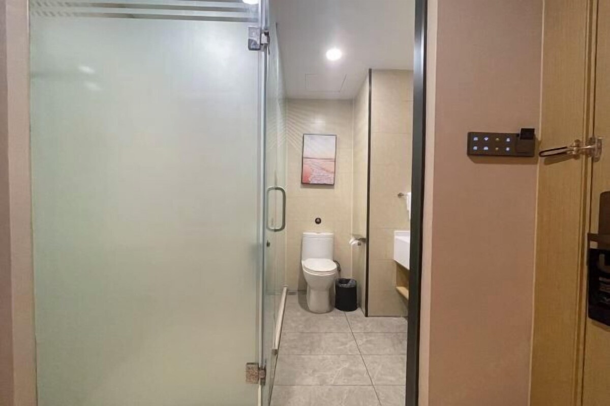 Un baño con cabina de ducha de vidrio, inodoro, cubo de basura y panel de control en la pared.