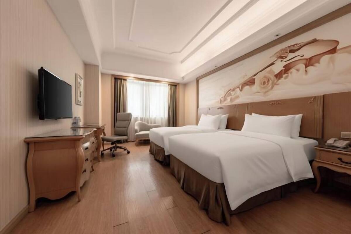 A hotel room with a bed, a desk, a chair, a television, and a painting on the wall.