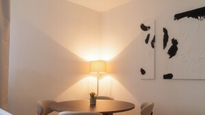 Una habitación de hotel con una mesa redonda, cuatro sillas, una lámpara y dos cuadros abstractos en la pared.