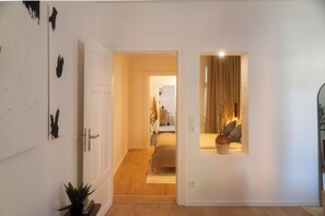 Ein Flur, der zu einem Schlafzimmer mit Bett, Nachttisch und Topfpflanze führt.
