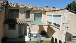 A stone house with a tiled roof, a small patio with a table and chairs, and a green umbrella. - Bienvenue Dans les Alpes de Hautes Provence . A Proximité des Gorges du Verdon (Beynes)