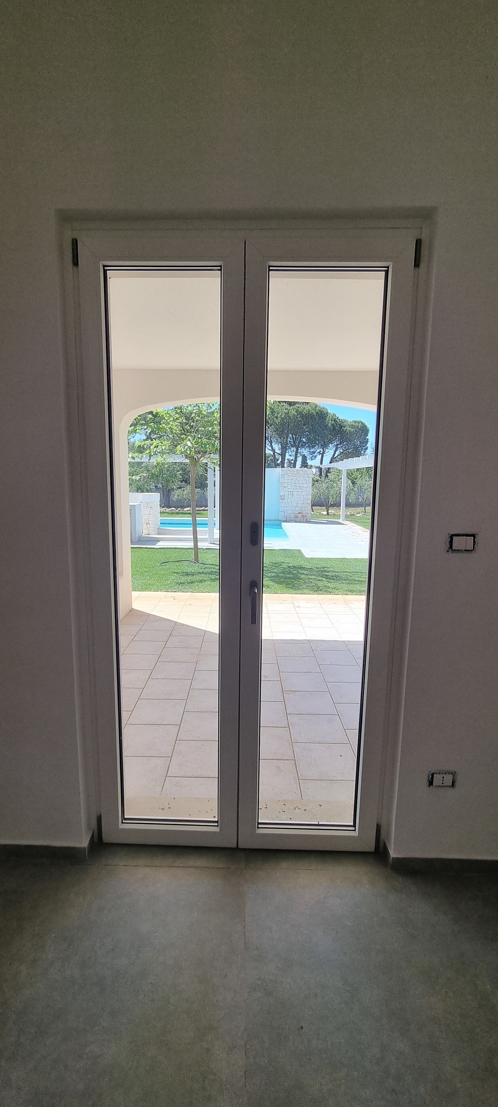 A room with a sliding glass door leading to an outdoor area with a pool and greenery.
