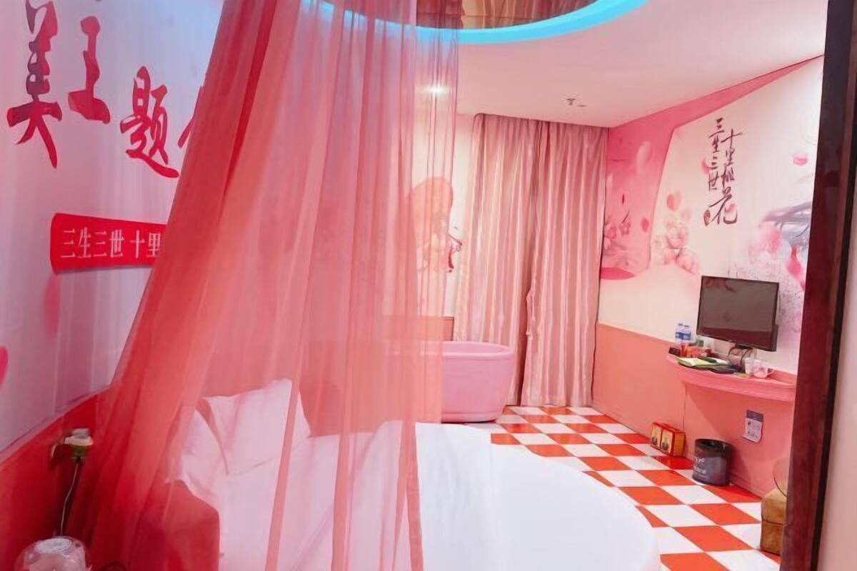 A hotel room with a bed, a TV, and a pink toilet.