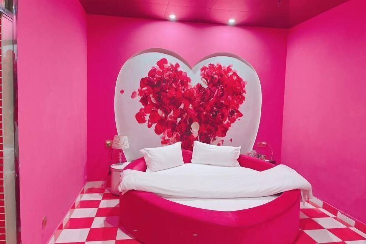 A room with a checkered floor, a bed with white bedding, and a wall with a heart-shaped floral design.