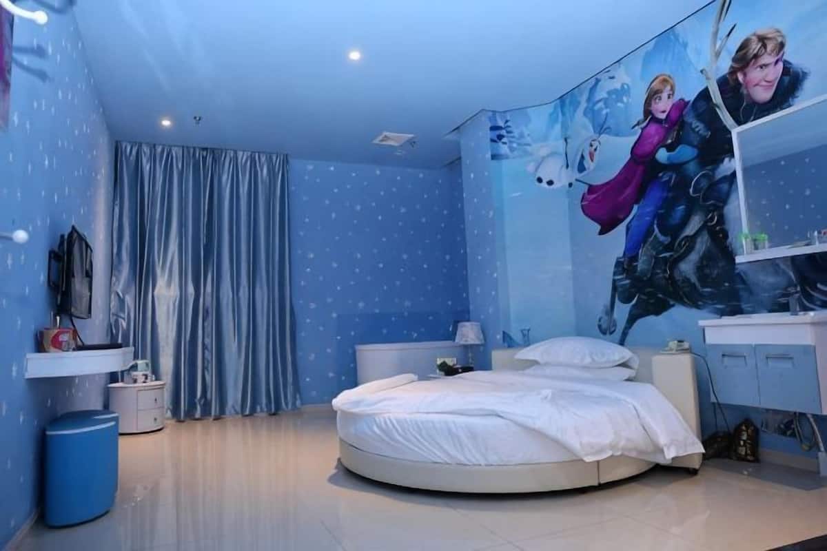 A bedroom with a round bed, a nightstand, a dresser, and a wall mural.
