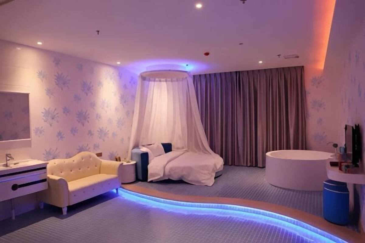 A bedroom with a bed, bedside table, and a round bathtub.
