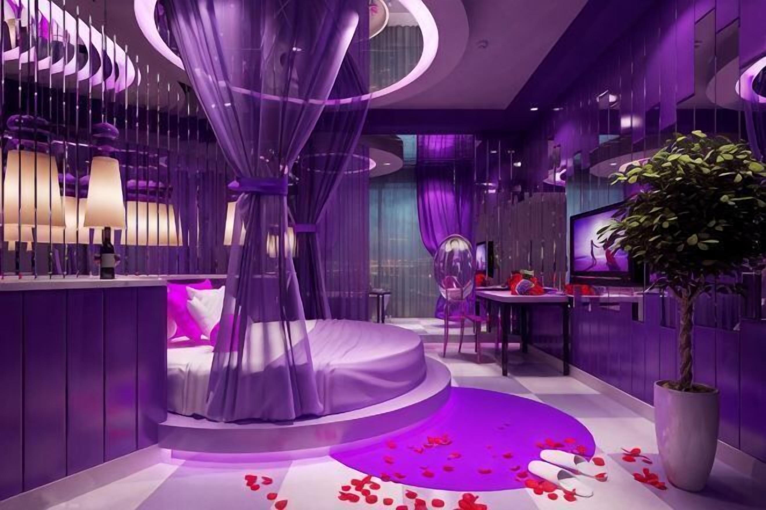 A modern hotel room with a circular bed, a large potted plant, and a purple-themed decor.