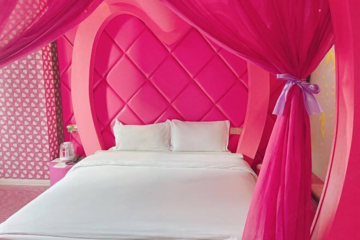 A bed with a white mattress and pillows, a pink headboard, and pink curtains.