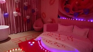 Un dormitorio con cama, almohadas, una mesita de noche y una cortina.