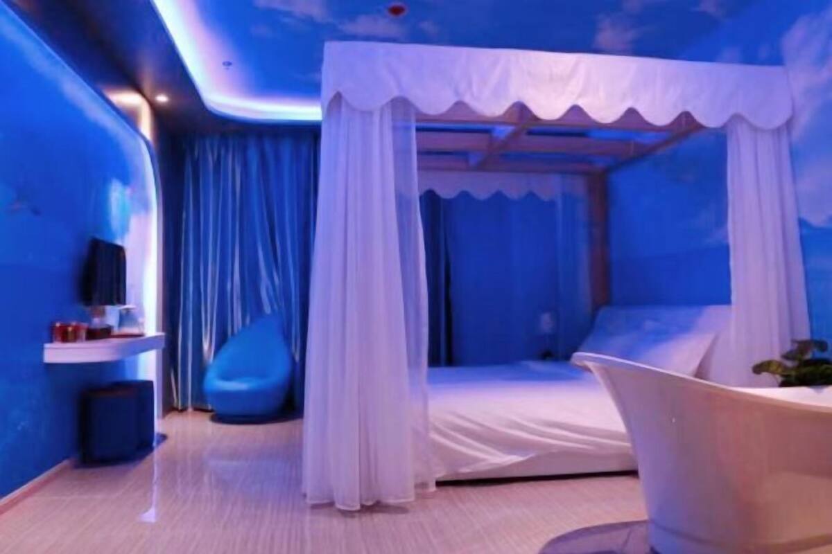 A room with a bed, a blue bean bag, a white bathtub, and a TV on a stand.