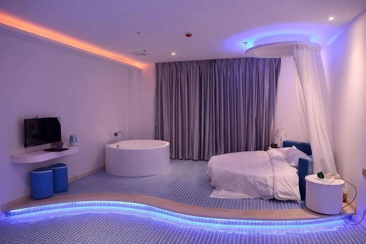 A modern bedroom with a bed, a bathtub, a TV, and a ceiling-mounted massage chair.
