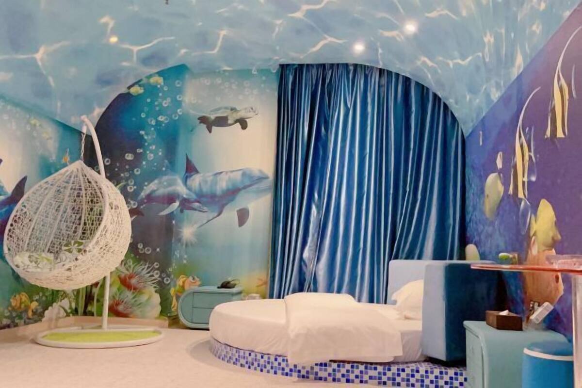 A room with a bed, a hanging chair, and a mural of underwater scenes.