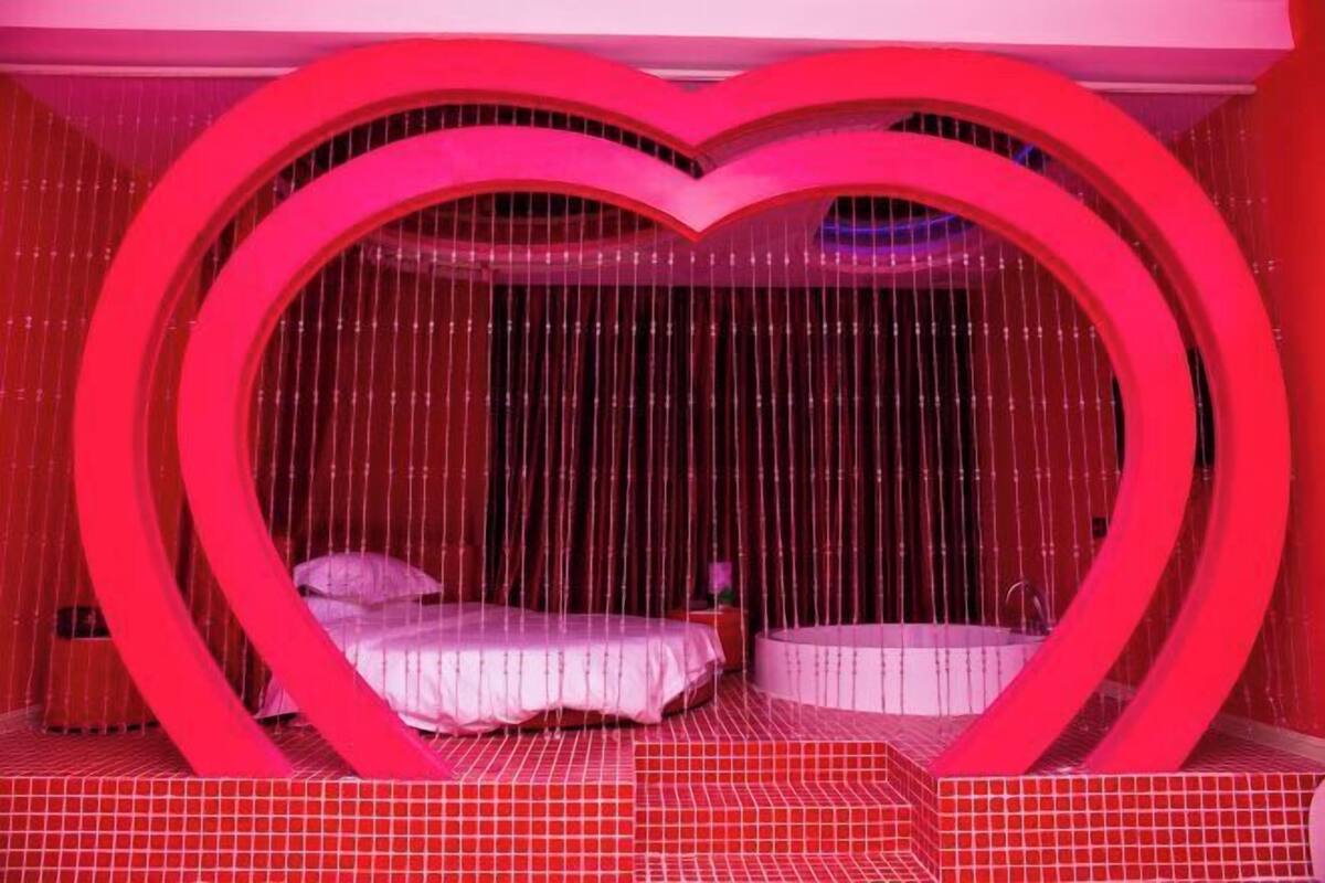 A room with a heart-shaped structure, a bed, and a small bathtub.