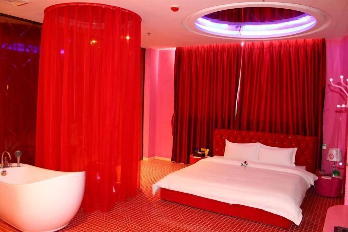 A red-themed hotel room with a large bed, a round ceiling light, and a bathtub.