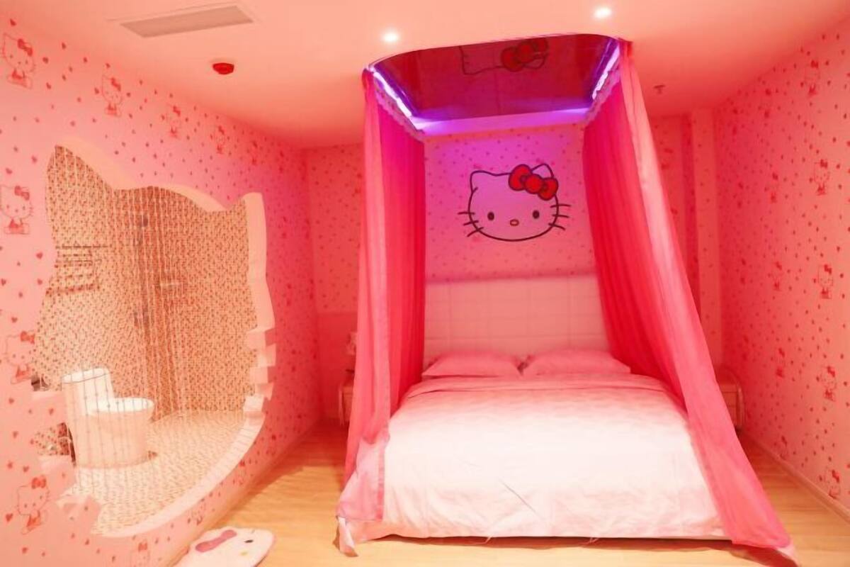 A pink-themed room with a Hello Kitty canopy bed, a white chair, and a small white table.