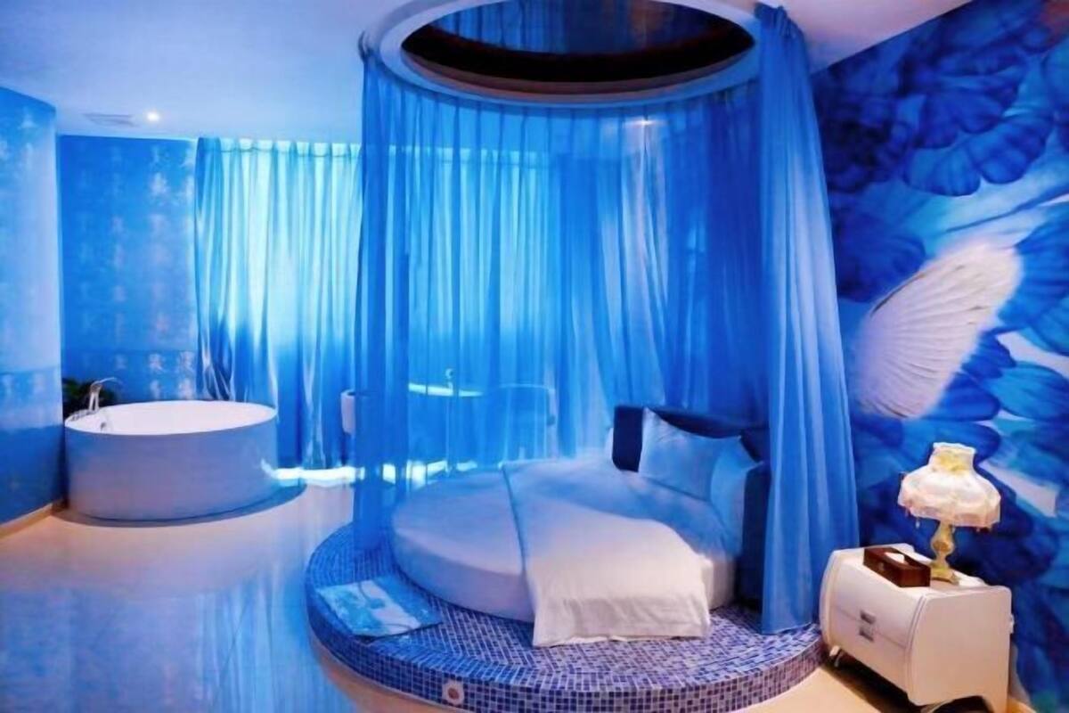 A bedroom with a round bed, a bathtub, and a canopy bed.