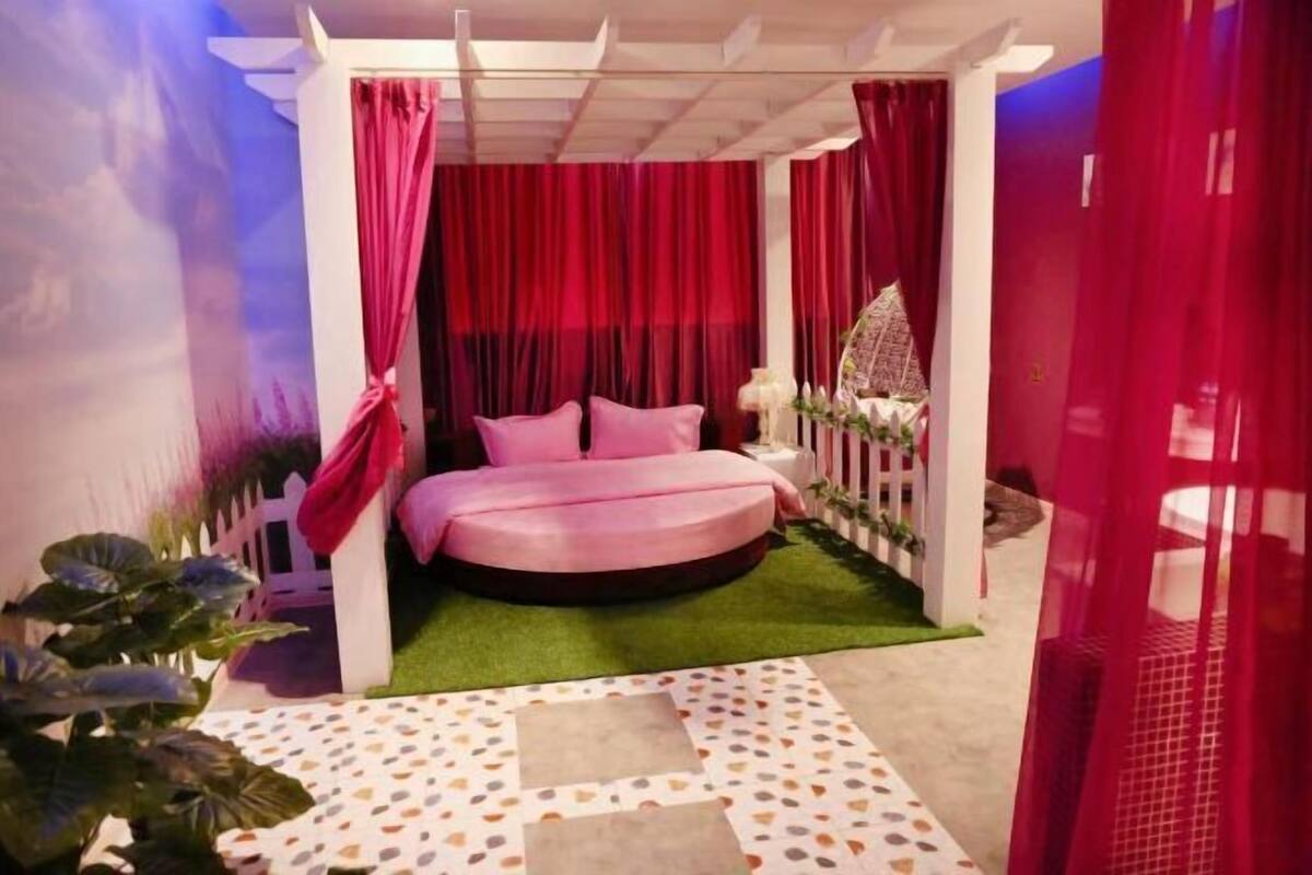 A circular bed with a green artificial grass floor, surrounded by red curtains and a white canopy.