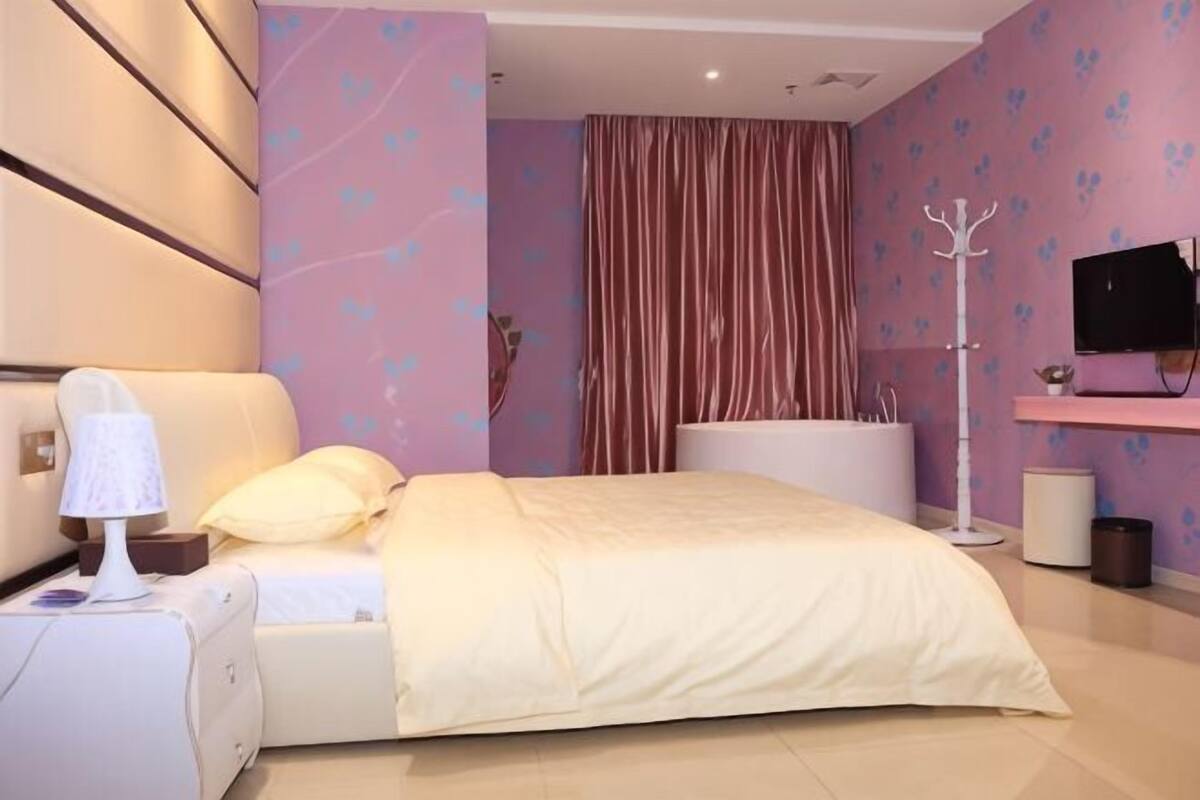 A bedroom with a bed, bedside table, lamp, and a television on a stand.
