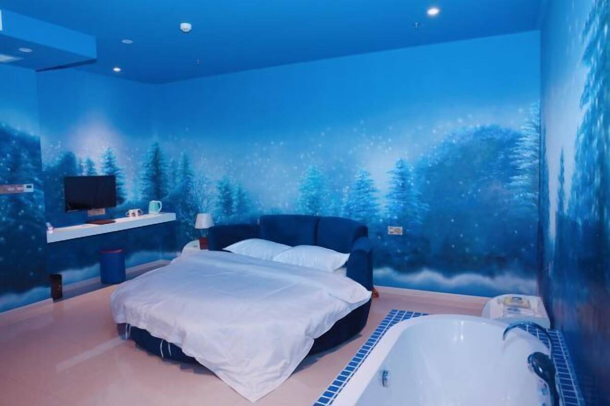 A bedroom with a bed, a nightstand, a TV, and a wall mural of a snowy forest.