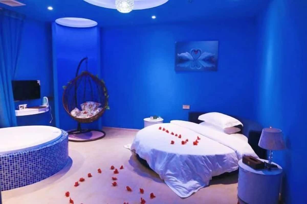 A bedroom with a bed, a hanging chair, a round bathtub, and a wall-mounted TV.
