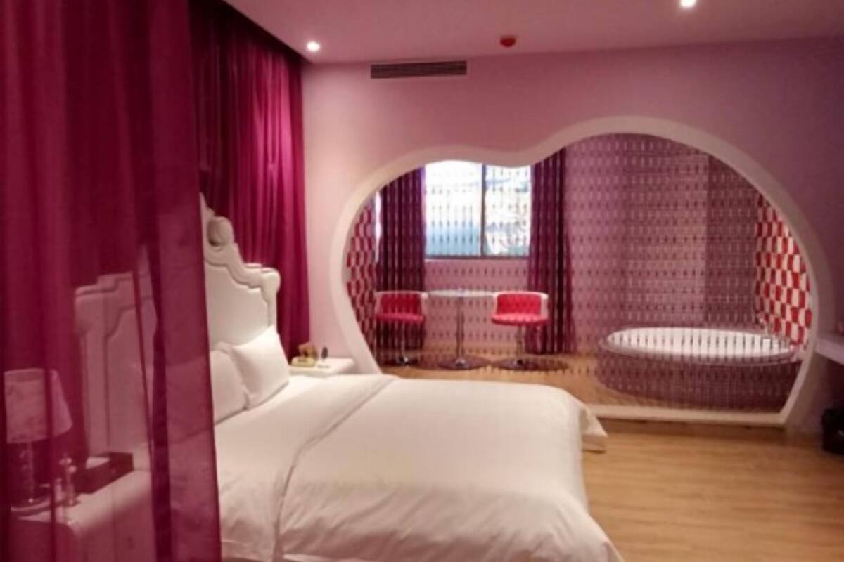 A bedroom with a bed, a circular seating area, and a window with patterned curtains.
