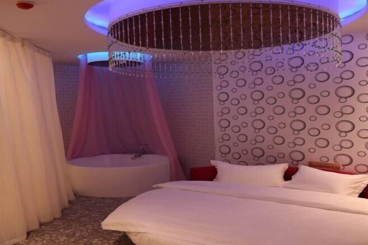 A bedroom with a bed, a circular window, a bathtub, and a chandelier.