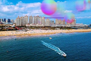 A coastal cityscape with a beachfront, high-rise buildings, and a boat on the water. - Qingdao Yijian Qingxin Whole Vision Apartment (Qingdao)