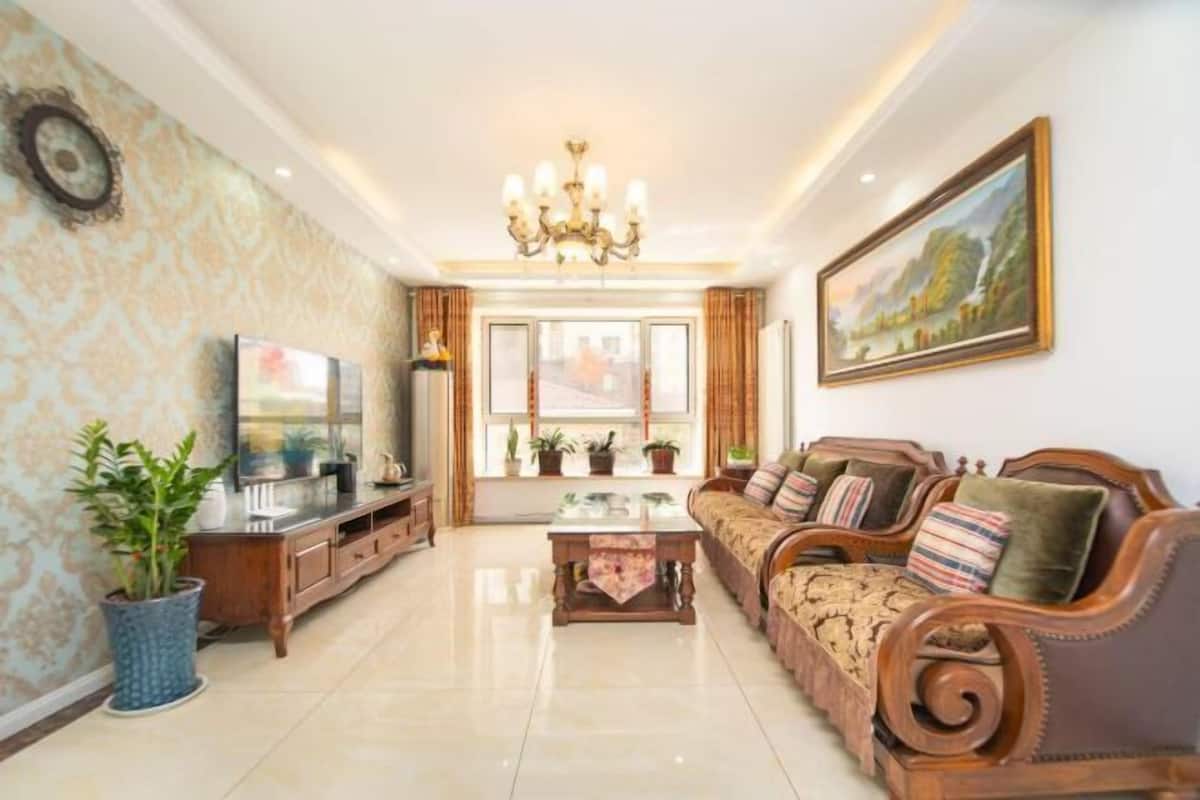 A spacious living room with a large sofa set, a TV, and a chandelier.