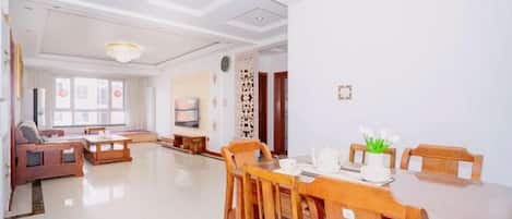 A spacious living room with a dining area, a sofa set, a TV, and a decorative wall.