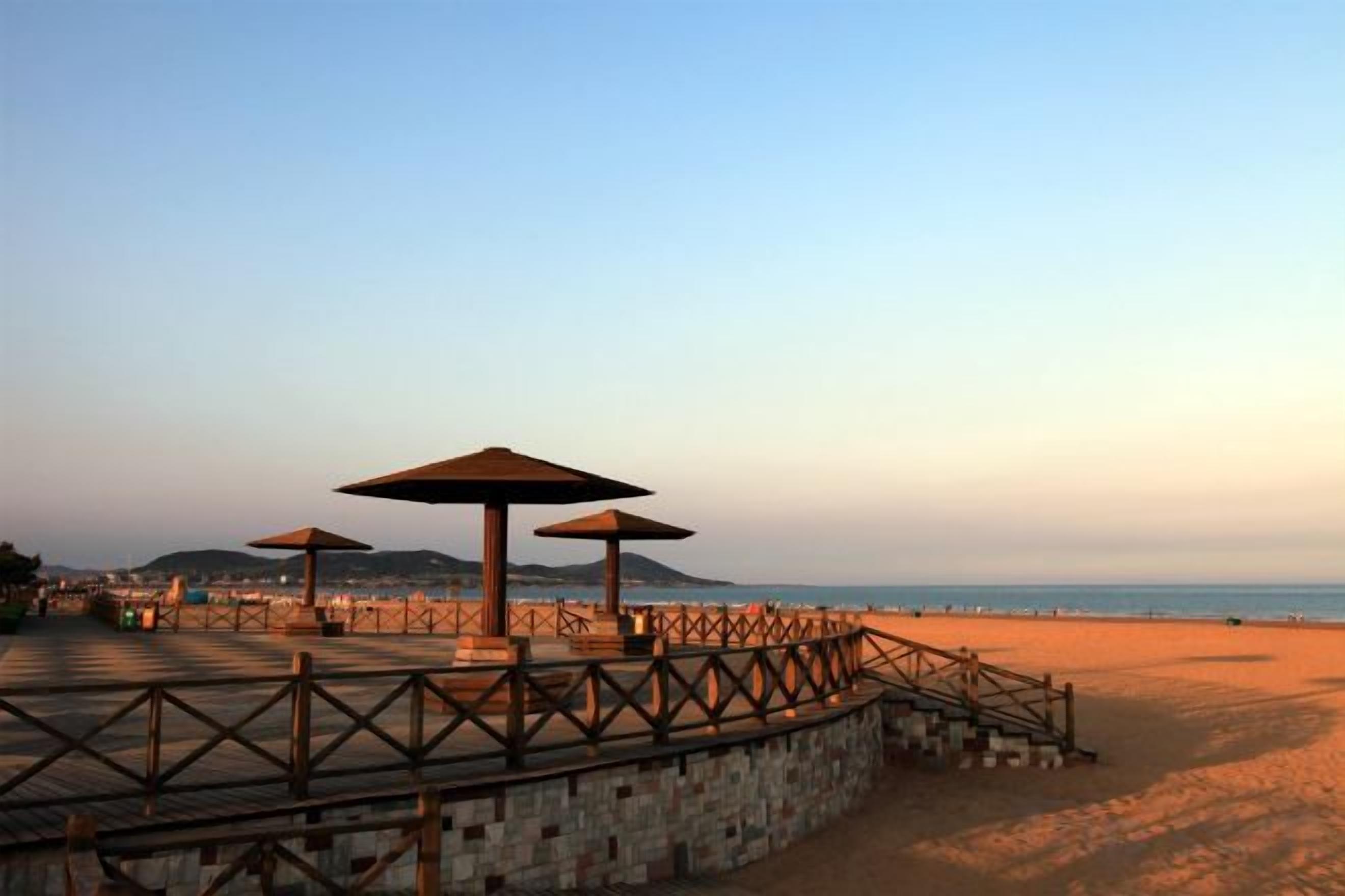A beach with a wooden walkway, stone walls, and three umbrellas.