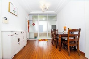 A dining area with a wooden table and chairs, a white cabinet, and a glass door leading to another room. - Qingdao Yijian Qingxin Whole Vision Apartment (Qingdao)