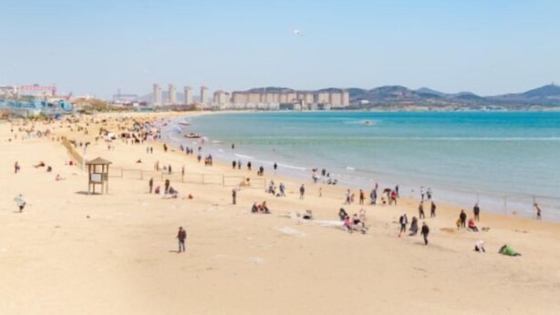 A beach with a lifeguard tower, sandy shore, and buildings in the background. - Qingdao Yijian Qingxin Whole Vision Apartment (Qingdao)