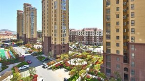 A high-rise residential building complex with multiple apartment buildings, a central courtyard with trees and greenery, and a parking area. - Qingdao Yijian Qingxin Whole Vision Apartment (Qingdao)