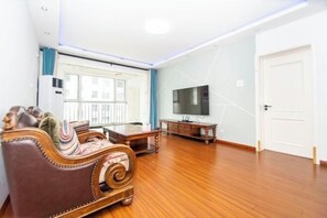 A living room with a sofa, a TV, a wooden floor, and a door. - Qingdao Yijian Qingxin Whole Vision Apartment (Qingdao)