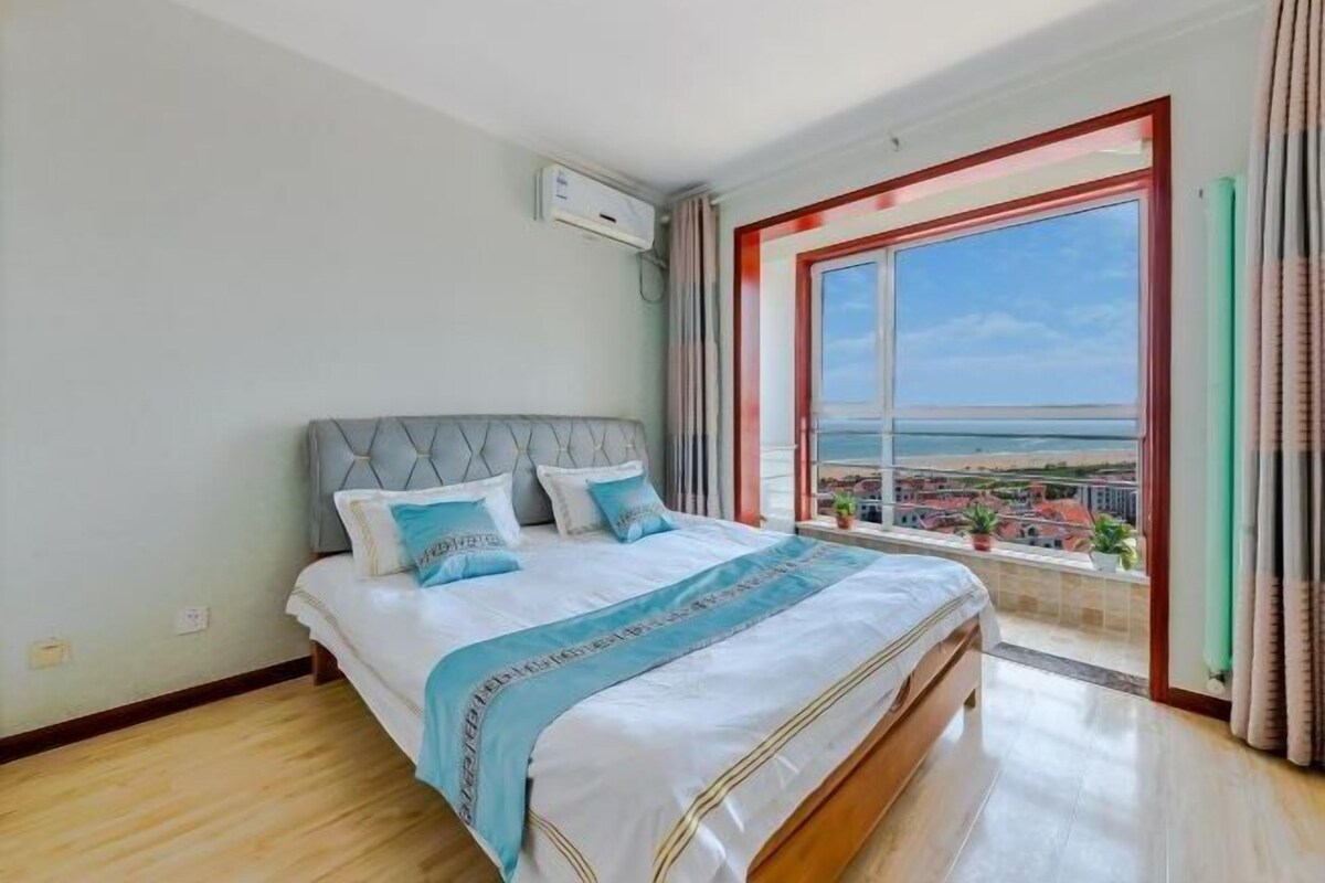 A bedroom with a bed, a window with a view, and an air conditioning unit.