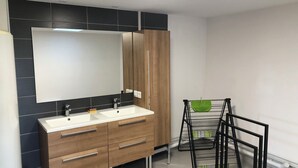Une salle de bain moderne avec un grand miroir, deux vasques, des meubles en bois et un porte-serviettes noir.
