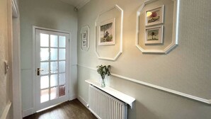 Ein Flur mit einer weißen Tür, einem Heizkörper und gerahmten Bildern an der Wand.