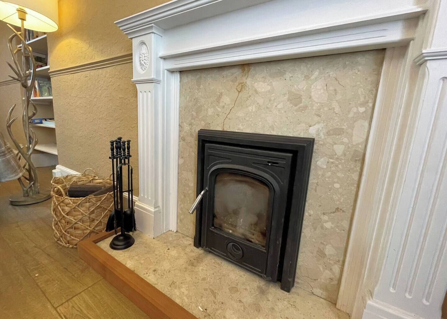 A fireplace with a stone surround, a black mantel, and a basket of firewood on the floor.
