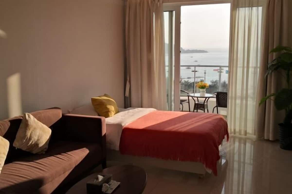 Ein Hotelzimmer mit Bett, einer Couch, einem kleinen Tisch und einem Balkon mit Meerblick.