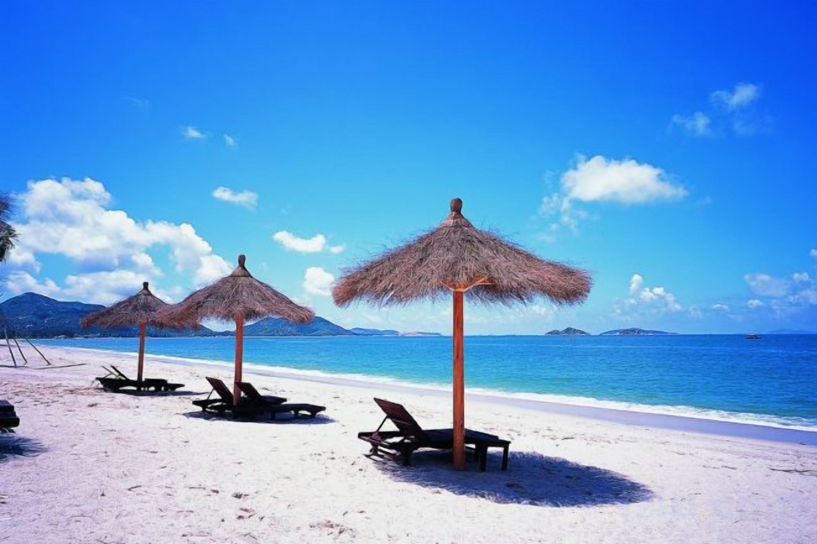 A beach with thatched umbrellas and lounge chairs.