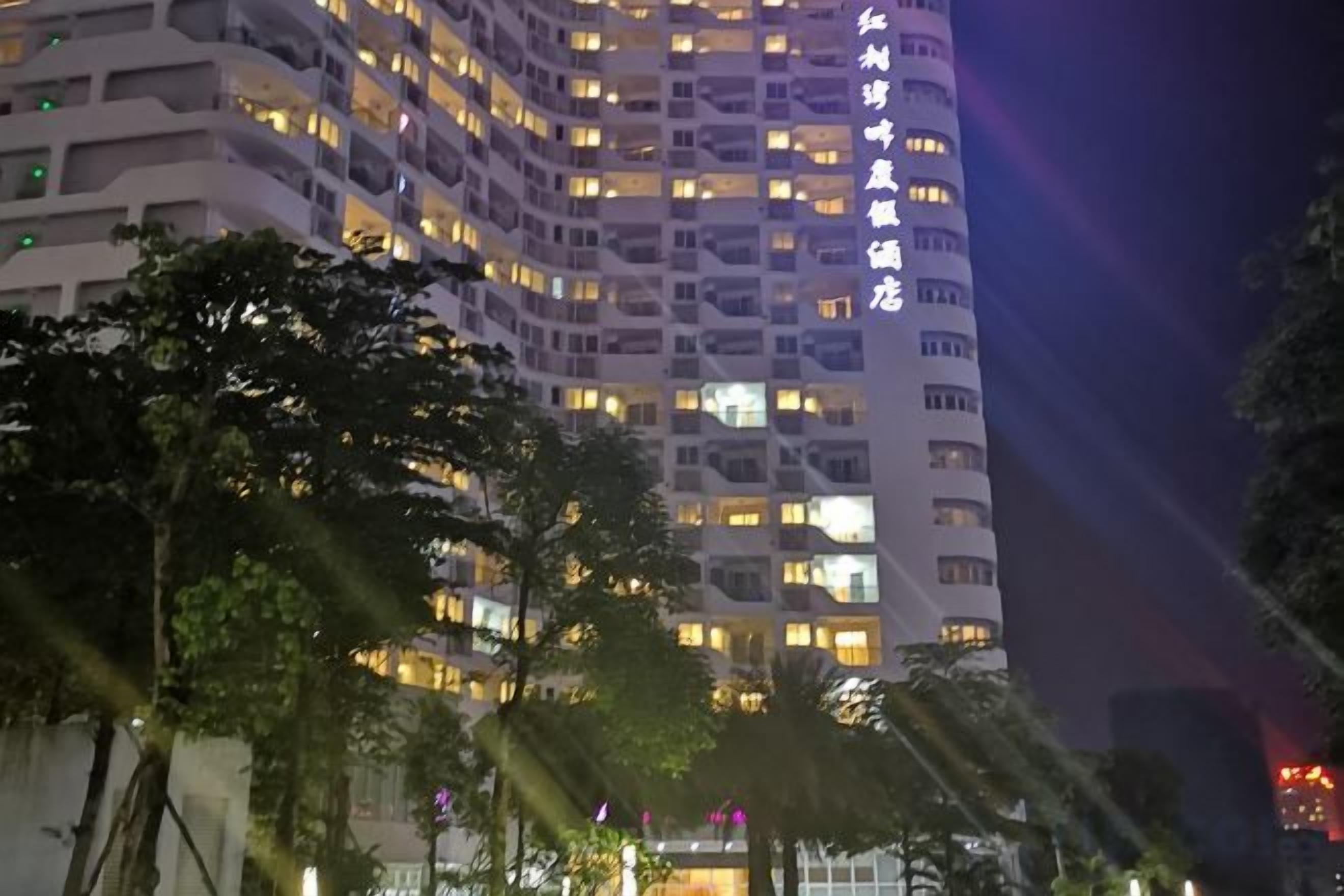 A multi-story hotel with illuminated windows and balconies, surrounded by trees.