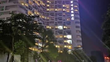 A multi-story hotel with illuminated windows and balconies, surrounded by trees.