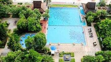 A large swimming pool with a leaf design, surrounded by lush greenery and shaded areas.