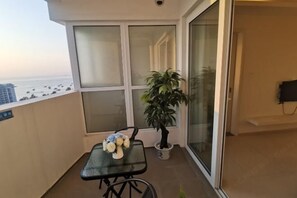 A balcony with a glass door, a small table with a vase of flowers, and a potted plant.