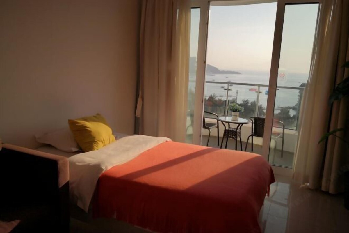 A hotel room with a bed, a small table, and a view of the sea through the balcony.
