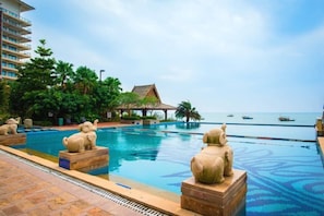 A swimming pool with decorative elephant statues, a building with a thatched roof, and a view of the sea with boats. - Hongshuwanpan Holiday Hotel (Huidong)