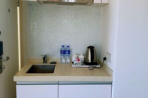 A small kitchen with a sink, a kettle, and two water bottles on the countertop.
